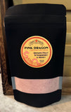 A black stand-up pouch of Pink Dragon Caffeine-Free Drink, Dragon Fruit Strawberry & Honey flavor, with a circular yellow and red label and a clear window showing the pink drink powder inside.